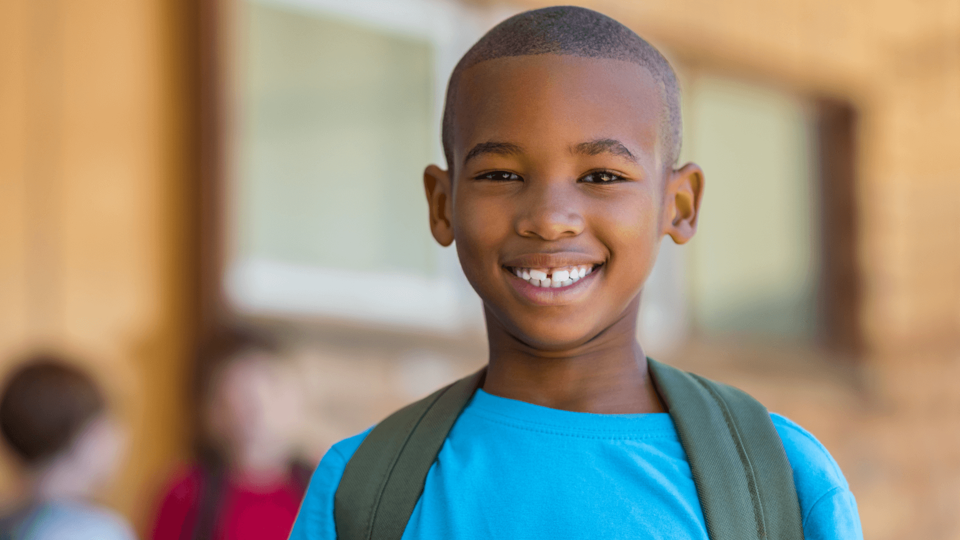 A cheerful young student with a backpack smiling in front of a school.